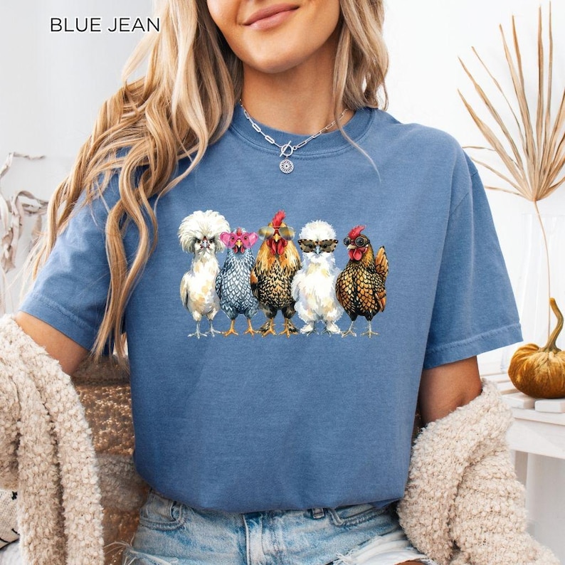May include: A blue jean colored t-shirt featuring a graphic print of five chickens standing in a row. Each chicken wears different colored sunglasses, including pink, black, and leopard print frames. The text BLUE JEAN is printed in the top corner.