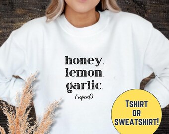 May include: White sweatshirt with the text "honey. lemon. garlic. (repeat)" and a yellow circle with the text "T-SHIRT OR SWEATSHIRT!"