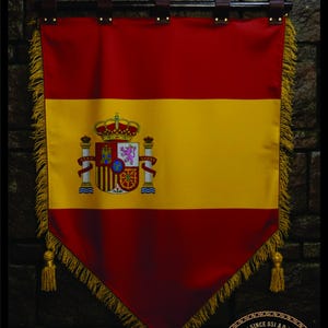 May include: A red, yellow, and red Spanish flag banner with a coat of arms in the center. The banner has a decorative fringe and tassels. The banner is hanging from a black rod with leather straps.