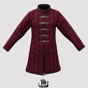 May include: A burgundy quilted coat with a high collar and long sleeves. The coat features brown leather accents and five buckle closures down the front. The coat is from East Coast Vikings.