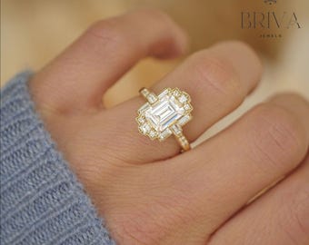 May include: A gold engagement ring with an emerald cut diamond center stone and a halo of smaller diamonds. The ring is set in a delicate, vintage-inspired design.