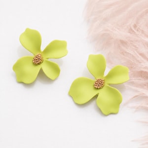 May include: A pair of lime green flower-shaped earrings featuring four rounded petals and a central cluster of small gold-toned beads. The earrings have a matte finish and a distinct four-petal design that mimics the appearance of a natural blossom.