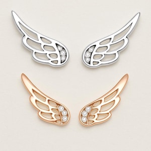 May include: Two pairs of wing-shaped earrings. One pair is silver-colored, and the other is rose gold. Each earring has a row of small, clear gemstones near the base. The wings have an open, detailed design.
