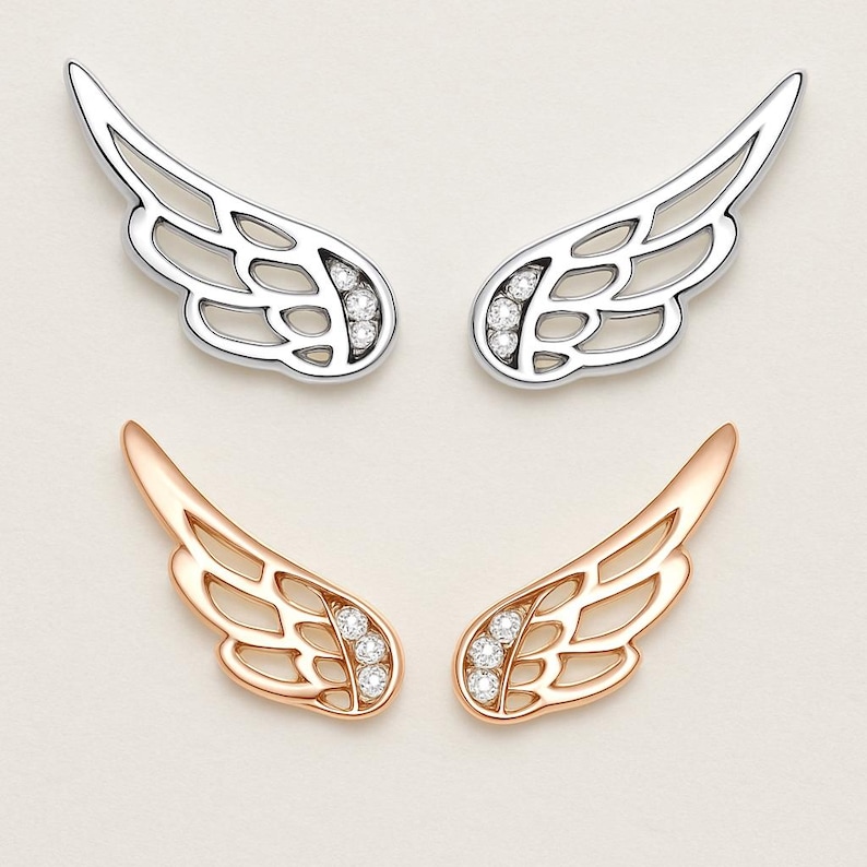 May include: Two pairs of wing-shaped earrings. One pair is silver-colored, and the other is rose gold. Each earring has a row of small, clear gemstones near the base. The wings have an open, detailed design.