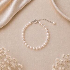 Puede incluir: Un delicado brazalete de perlas con cierre y cadena extensora de plata. El brazalete est&aacute; compuesto por numerosas perlas peque&ntilde;as, redondas y de color blanco crema. El fondo es beige suave con acentos florales.