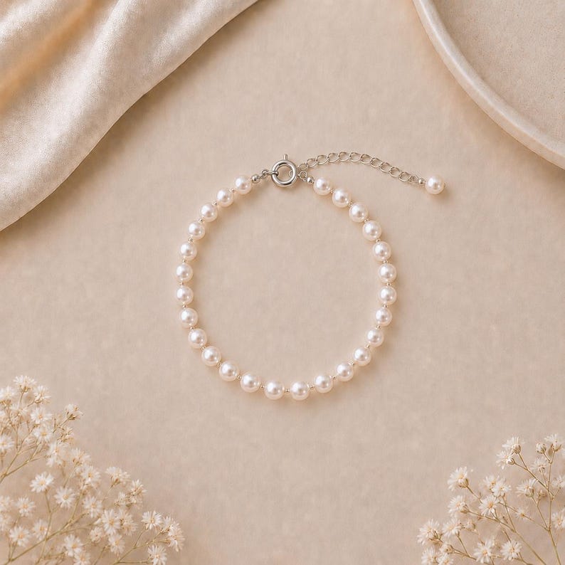 Puede incluir: Un delicado brazalete de perlas con cierre y cadena extensora de plata. El brazalete est&aacute; compuesto por numerosas perlas peque&ntilde;as, redondas y de color blanco crema. El fondo es beige suave con acentos florales.
