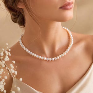 Puede incluir: Un delicado collar de perlas con un dise&ntilde;o cl&aacute;sico. El collar presenta una hilera de perlas redondas y lustrosas, creando un aspecto atemporal y elegante. Las perlas son de color blanco cremoso y el collar se lleva cerca del cuello.