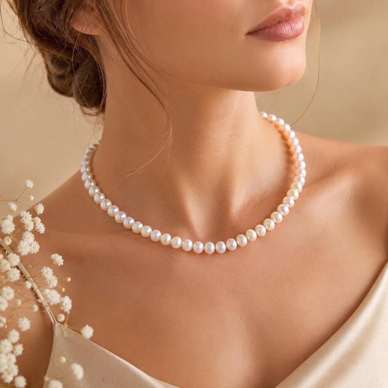 Puede incluir: Un delicado collar de perlas con un dise&ntilde;o cl&aacute;sico. El collar presenta una hilera de perlas redondas y lustrosas, creando un aspecto atemporal y elegante. Las perlas son de color blanco cremoso y el collar se lleva cerca del cuello.