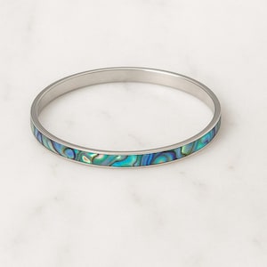 May include: A silver-toned bangle bracelet with an iridescent abalone shell inlay. The inlay features swirling patterns of blue, green, and teal. The bracelet is a simple, elegant design.