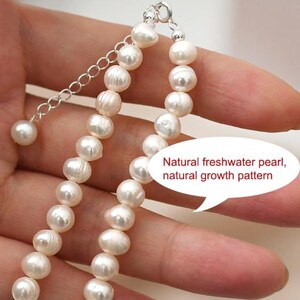 Puede incluir: Primer plano de un collar de perlas con cadena y cierre plateados. El collar est&aacute; hecho de perlas blancas y redondas. El texto de la imagen dice: "Perla natural de agua dulce, patr&oacute;n de crecimiento natural."