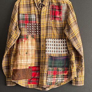 Op de afbeelding: Een button-down overhemd met lange mouwen en een geel-bruin ruitpatroon. Het overhemd heeft verschillende stoffen patches in rood, groen en bruin, waardoor een uniek patchwork-ontwerp ontstaat. De kraag heeft een label met "DANI STAR".