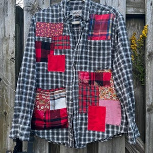 May include: A long-sleeve button-down shirt featuring a black and white plaid pattern with various rectangular fabric patches in red, floral, and checkered prints sewn onto the front. The shirt has a collar and a label reading DANI.