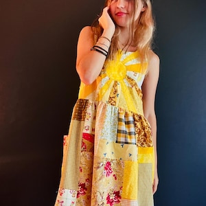 Könnte beinhalten: Ein Patchwork-Kleid in Gelb-, Weiß- und floralen Mustern. Das ärmellose Kleid hat ein Sonnenmuster auf dem Oberteil und einen ausgestellten Rock. Das Kleid besteht aus verschiedenen Stoffquadraten, die zusammengenäht wurden, wodurch ein einzigartiges und farbenfrohes Design entsteht.