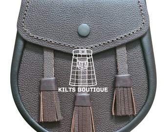 May include: A brown leather sporran with a flap closure and three decorative tassels. The sporran has a textured surface and a button closure. The text "KILTS BOUTIQUE" is printed on the front.