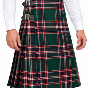 Puede incluir: Una falda escocesa plisada con un patrón de tartán en verde oscuro, azul marino, blanco y rojo. La prenda incluye dos correas de cuero negro ajustables con hebillas de metal plateado en el lateral para un ajuste seguro en la cintura.
