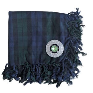 May include: A navy blue and green plaid kilt with a silver brooch featuring a green gemstone center. The kilt has a fringed edge in matching colors. The brooch is round with an intricate Celtic knot design.