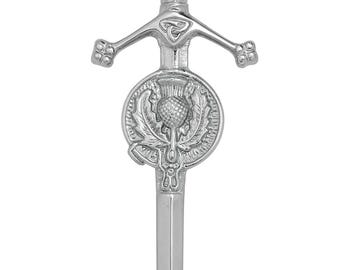 May include: A silver kilt pin, featuring a thistle emblem within a circular frame. The pin has a decorative hilt and a twisted handle. The design is symmetrical and the pin is likely made of metal.