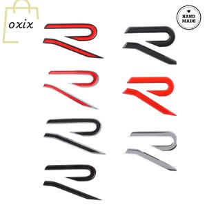 Peut inclure: Plusieurs emblèmes de la lettre "R" stylisée en rouge, noir et argent. Les emblèmes sont présentés sur fond blanc. Le mot "oxix" est dans le coin supérieur gauche, et un autocollant "Hand Made" est dans le coin supérieur droit.