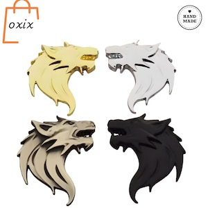 Puede incluir: Cuatro emblemas de cabeza de lobo metálicos en dorado, plateado, gris y negro. Cada emblema presenta un diseño detallado de cabeza de lobo con dientes afilados y una melena fluida. Los emblemas son probablemente para fines decorativos.