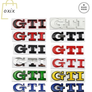 Puede incluir: Una colección de insignias de emblema de coche GTI en varios colores, incluyendo rojo, negro, blanco, verde, amarillo y azul. Cada insignia es rectangular con las letras GTI.