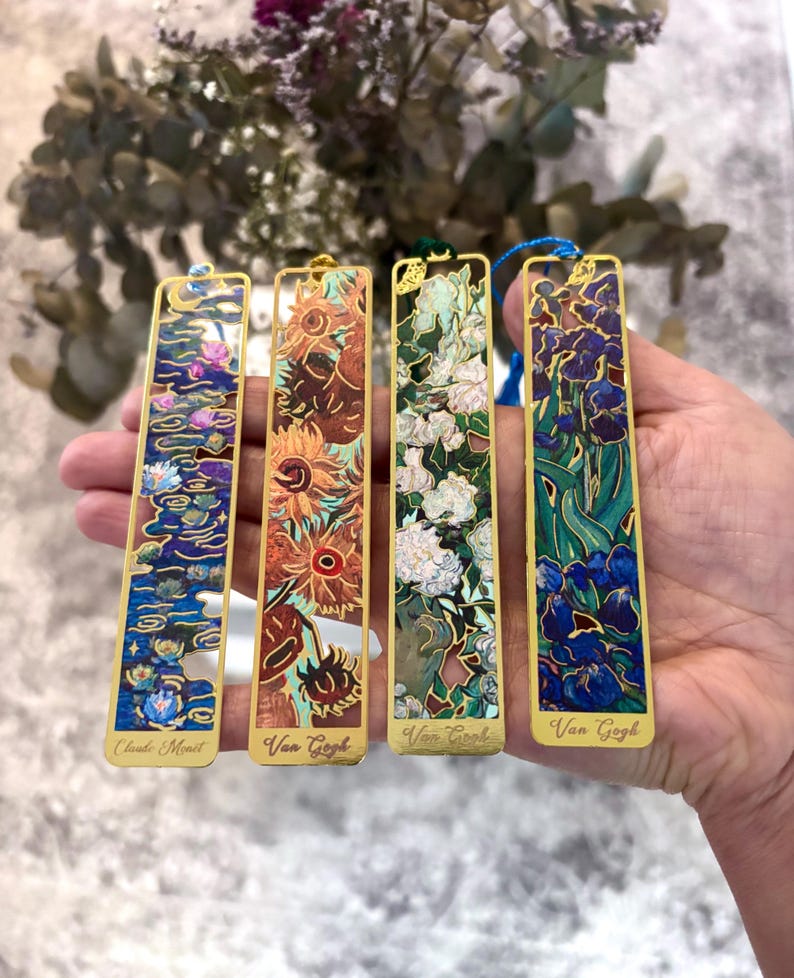 May include: Four gold-toned metal bookmarks featuring famous art. One depicts water lilies by Claude Monet, and three feature sunflowers and irises by Van Gogh. Each bookmark has a colorful, detailed design and a small tassel.