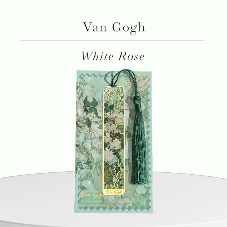 May include: A gold-colored metal bookmark featuring a floral design with a green tassel. The bookmark is set against a green background with the text "Van Gogh White Rose". The design includes white roses and green leaves.