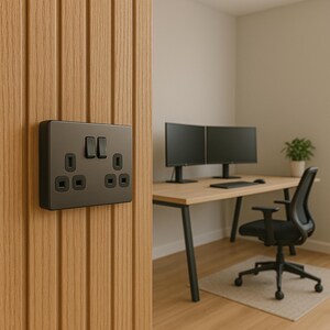 May include: A dark gray electrical outlet and light switch are mounted on a vertical wooden panel. The outlet has two plug receptacles and a switch. The background shows a desk with two computer monitors, a keyboard, and a chair.