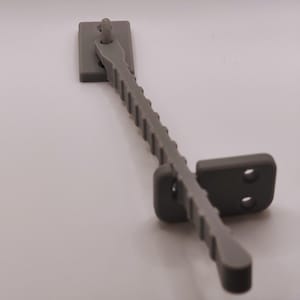 K&ouml;nnte beinhalten: Ein grauer Fensterriegel aus Kunststoff. Er hat eine rechteckige Basis, einen geriffelten Arm und ein zweites rechteckiges Teil mit zwei L&ouml;chern. Der Arm ist angelenkt. Dieser Riegel dient zur Sicherung eines Fensterfl&uuml;gels.