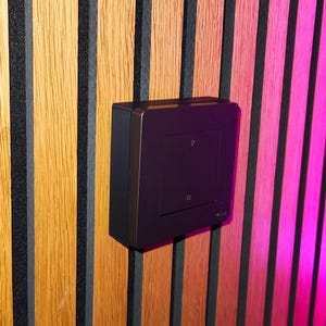 Peut inclure: Un interrupteur de lumière carré et sombre avec une petite icône d'ampoule et une icône zéro est monté sur un mur en bois. Le mur est composé de planches de bois verticales dans des tons de marron et de noir. L'interrupteur a une finition métallique.