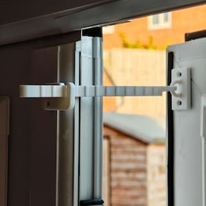 May include: A white plastic window and door safety lock. The lock has a sliding bar with multiple notches that connects to a fixed base. The lock is designed to limit how far a window or door can open.