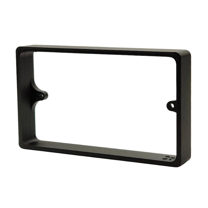 May include: A black rectangular frame with rounded corners and mounting holes. The frame has a smooth, matte finish and a hollow center. The frame is designed to hold a rectangular object.