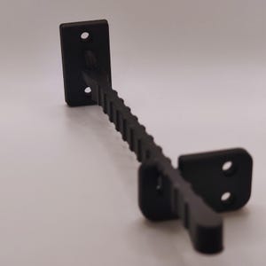 K&ouml;nnte beinhalten: Eine schwarze Metallhalterung mit einer rechteckigen Montageplatte und einem strukturierten, abgewinkelten Arm. Die Halterung hat zwei L&ouml;cher in der Montageplatte und zwei L&ouml;cher in der anderen Platte.
