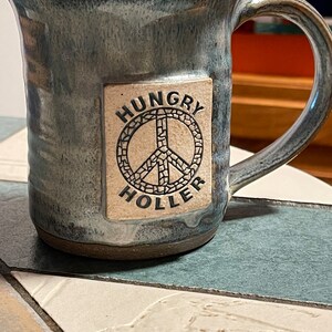 May include: A blue ceramic mug with a white peace sign and the text "Hungry Holler" on the side.