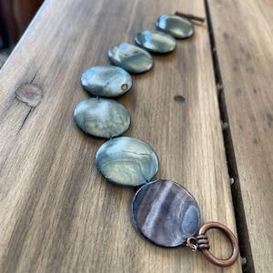 May include: A bracelet made of round, gray and black shell beads with a copper clasp.
