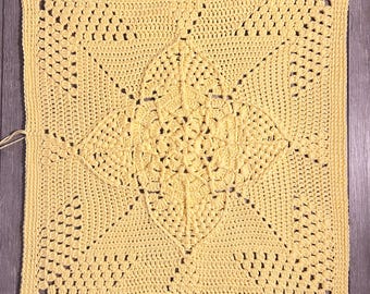 May include: A yellow crocheted square blanket with a detailed, intricate pattern in the center.