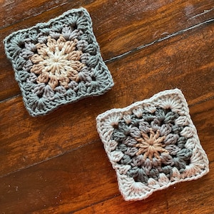 May include: Two crocheted squares with a brown and gray color scheme. The squares have a flower-like design in the center.