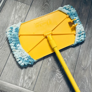 May include: Yellow and blue mop with a long yellow handle. The mop head is made of a soft, fluffy material and has the word "Quickie" printed on the yellow frame.