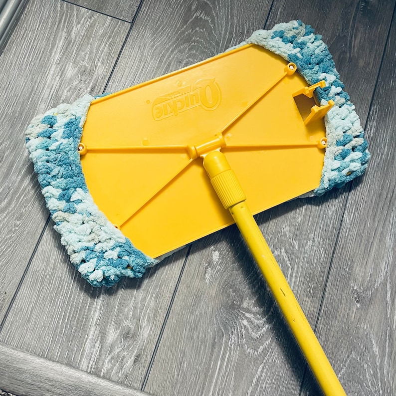 May include: Yellow and blue mop with a long yellow handle. The mop head is made of a soft, fluffy material and has the word "Quickie" printed on the yellow frame.
