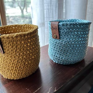 May include: Two crocheted baskets, one yellow and one blue, with leather tags that say "S&S".