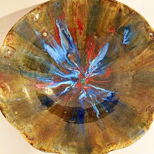 Könnte beinhalten: Eine handgefertigte Keramikschale mit einem einzigartigen, abstrakten Design. Die Schale zeigt eine Mischung aus braunen, blauen und roten Farben, die einen auffälligen visuellen Effekt erzeugt. Der Rand hat eine wellenförmige Kante, die ihren künstlerischen Reiz verstärkt. Ideal zum Servieren oder Dekorieren.