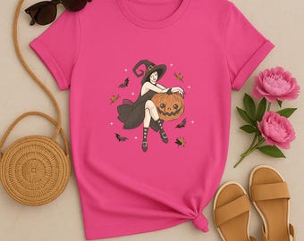 Może przedstawiać: Różowa koszulka z ilustracją na Halloween. Grafika przedstawia wiedźmę z dynią, nietoperzami i liśćmi. Koszulka ma podwinięte rękawy i wiązany dół. Akcesoria: okulary przeciwsłoneczne, słomiana torba i sandały.
