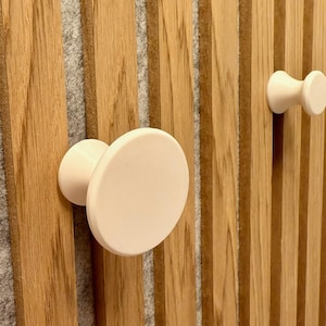 Peut inclure: Deux boutons en céramique blanche montés sur un panneau en bois avec des rainures verticales. Les boutons sont de tailles et de formes différentes.