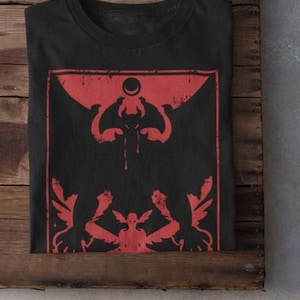 May include: Black t-shirt with a red graphic print of a winged creature with a crescent moon above it. The creature has a dripping teardrop from its eye.