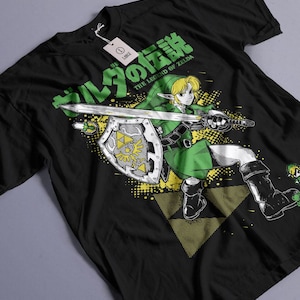 Puede incluir: Camiseta negra con un gráfico de un personaje de The Legend of Zelda, empuñando una espada y un escudo. El diseño incluye texto japonés y las palabras "THE LEGEND OF ZELDA" en verde. Una etiqueta blanca con la talla "L" cuelga de la camiseta.