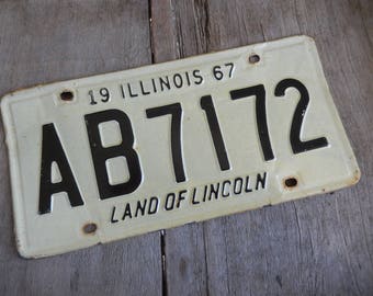 May include: A white vintage Illinois license plate with black lettering. The plate reads "19 ILLINOIS 67 AB7172 LAND OF LINCOLN".