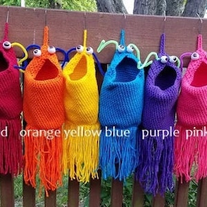 May include: Six crocheted hanging pockets in rainbow colors, red, orange, yellow, blue, purple, and pink, with googly eyes and pipe cleaner antennae.