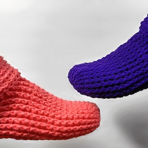 Könnte beinhalten: Zwei Paar gestrickte Hausschuhe, eines in Pink und eines in Lila. Die Socken sind oben umgeklappt und haben eine gerippte Struktur.