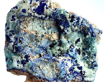 May include: A rough, natural rock specimen with a mix of blue, green, and white colors. The rock has a rough, textured surface and is covered in small crystals.