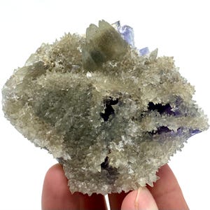 May include: A natural mineral specimen featuring a cluster of crystalline formations. The piece showcases a mix of colors, including clear, light green, and hints of purple. The crystals have a spiky, textured appearance.