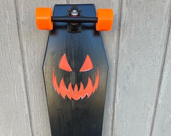 May include: A black longboard skateboard with orange wheels and a jack-o'-lantern design on the deck.